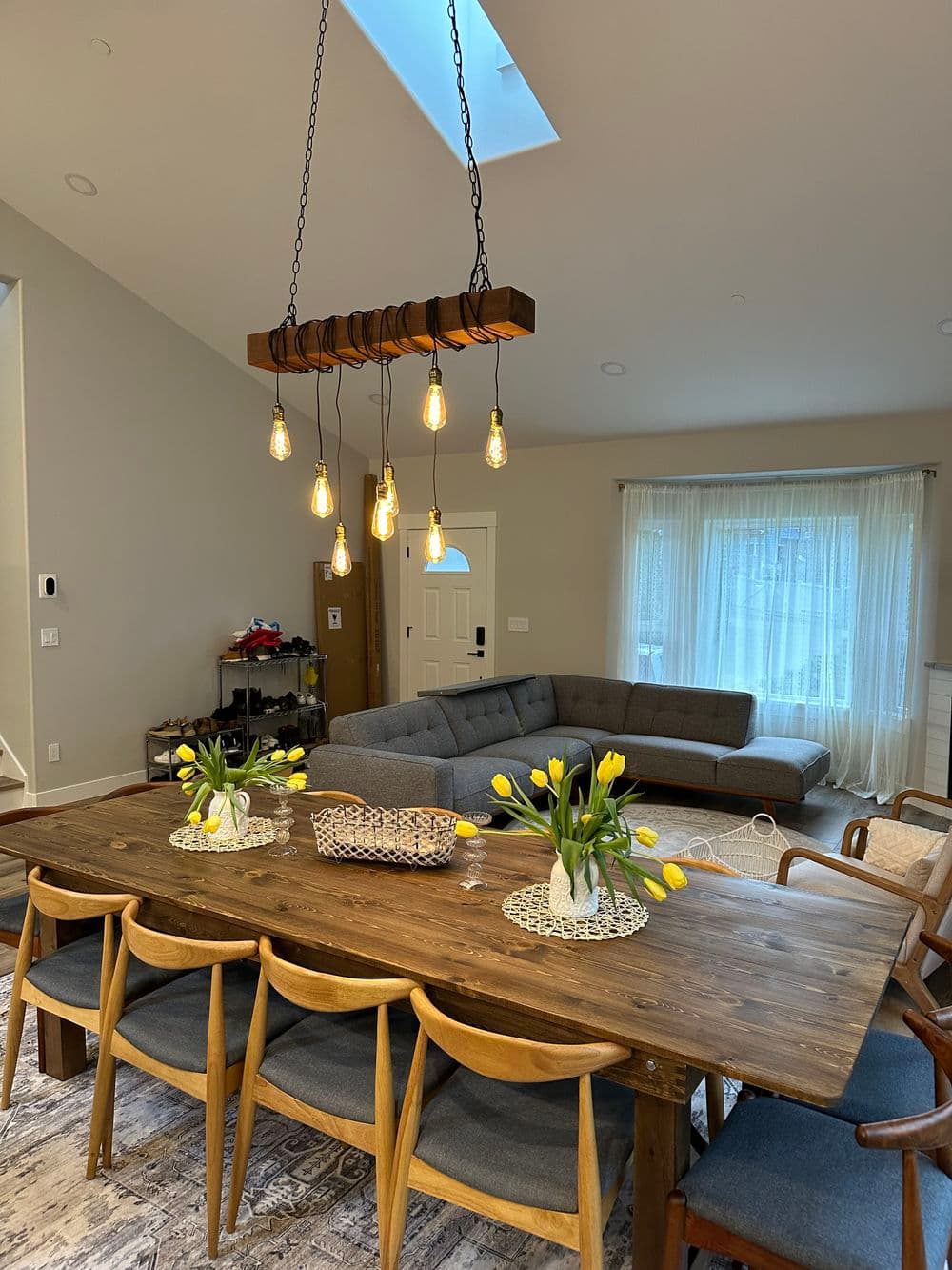 Modern dining room with wooden table, vintage light fixture, and fresh tulips in vases.