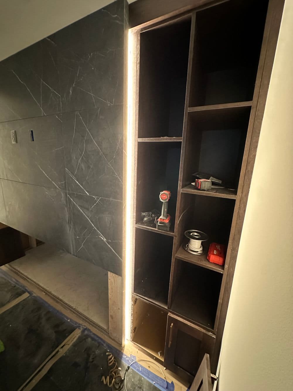 Modern cabinet installation with tools, featuring sleek dark panels and LED lighting.