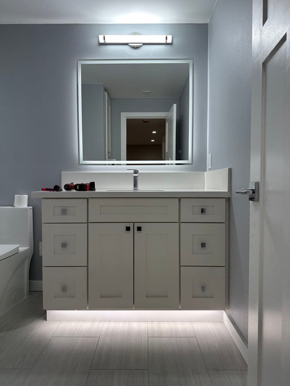 Modern bathroom with white vanity, large mirror, and stylish lighting accents.