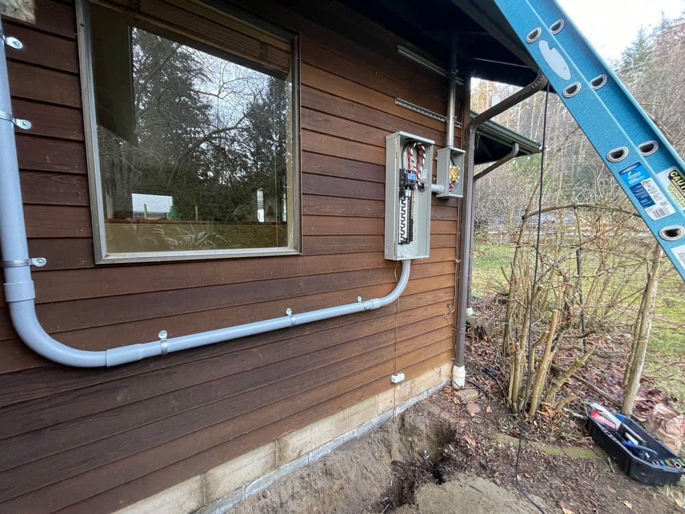 Electrical panel installed on a wooden cabin exterior with ladder and conduit.