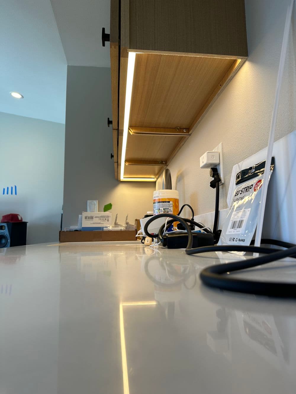 Modern kitchen countertop with under-cabinet lighting, appliances, and various cables.