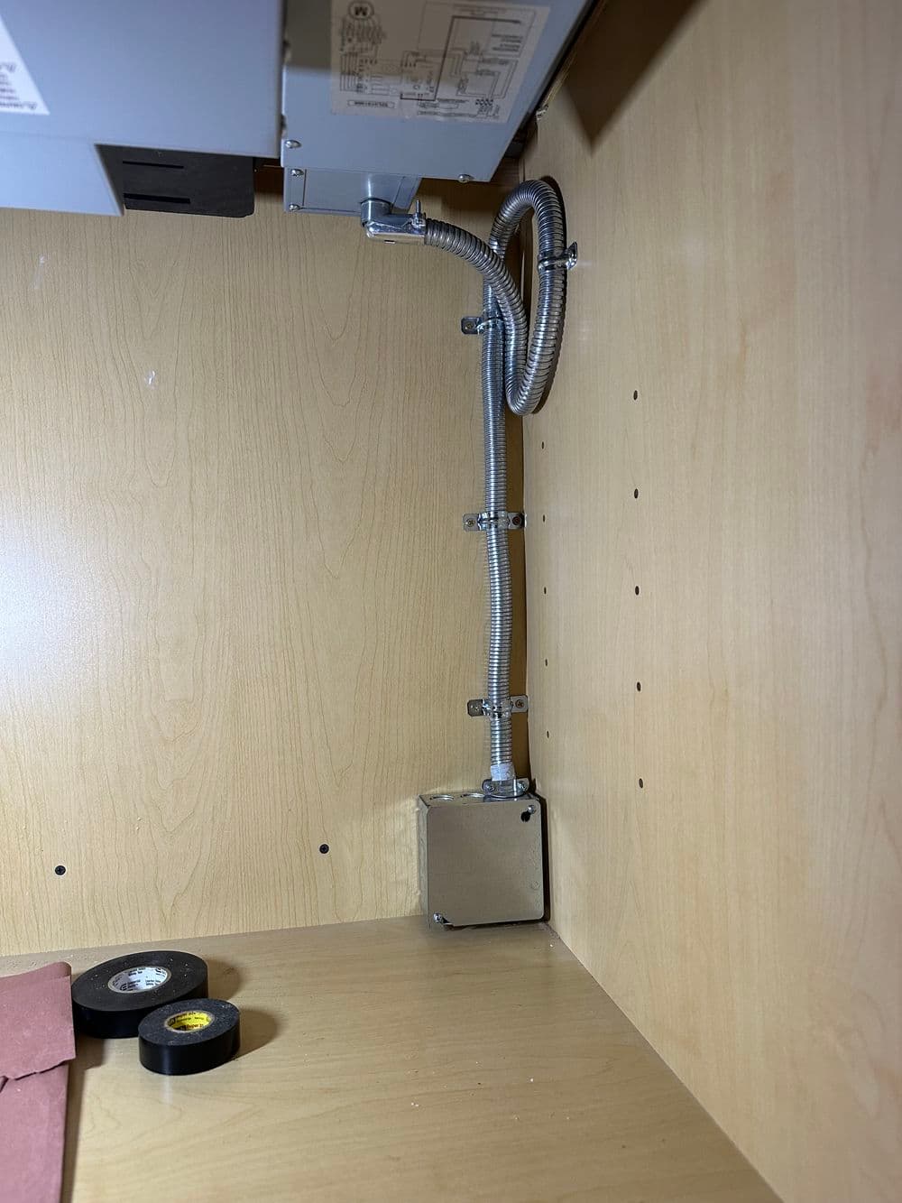 Electrical conduit and junction box installed in a wooden cabinet for wiring. Tools nearby.
