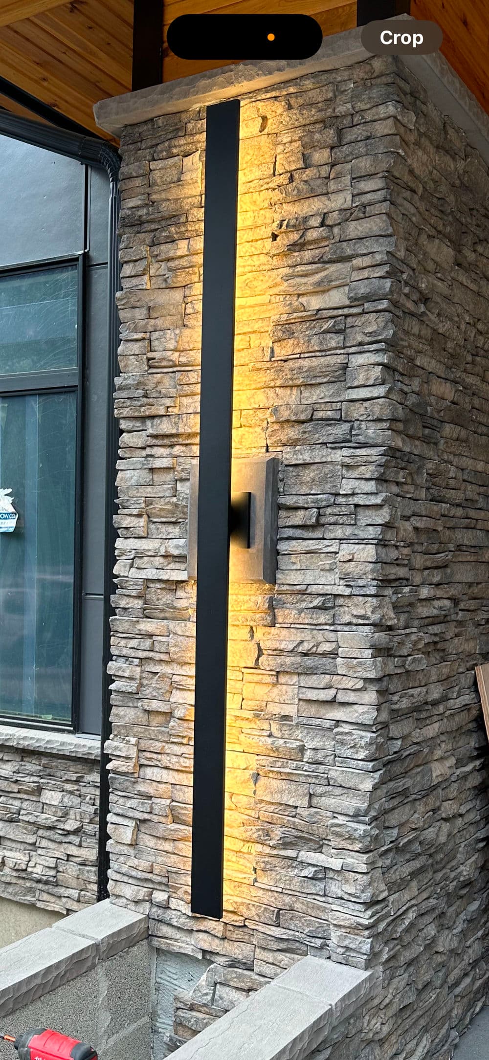 Modern vertical outdoor light fixture on a stone wall, highlighting architectural features.