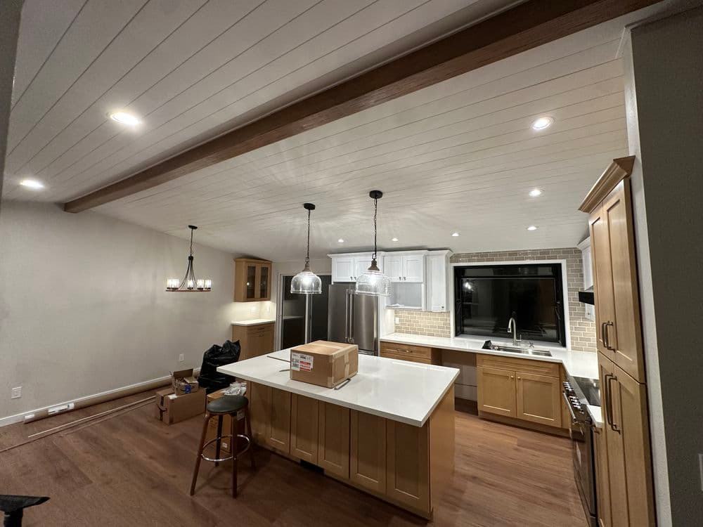 Modern kitchen renovation featuring white cabinets, large island, and wooden accents.