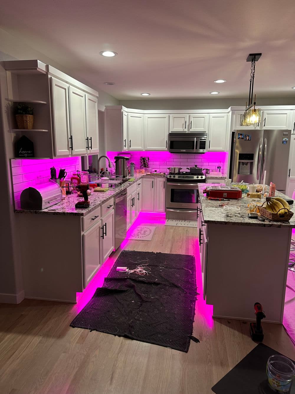 Modern kitchen with pink LED lights, white cabinets, granite countertops, and a cozy ambiance.