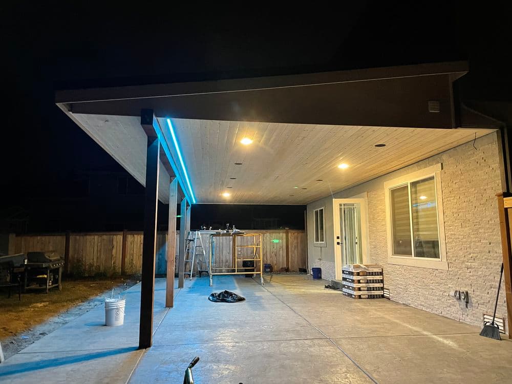Modern patio with illuminated ceiling, outdoor lighting, and concrete flooring at night.