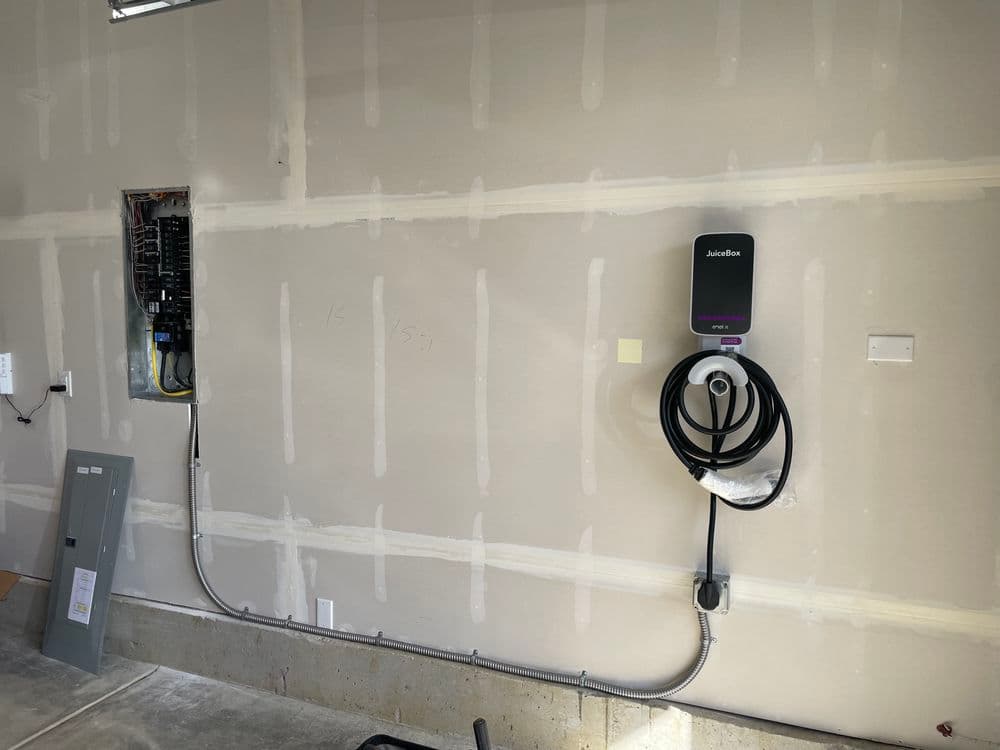 Electric vehicle charger installed on a garage wall next to an electrical panel.
