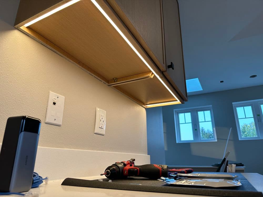 Kitchen under-cabinet lighting installation with tools and materials on countertop.