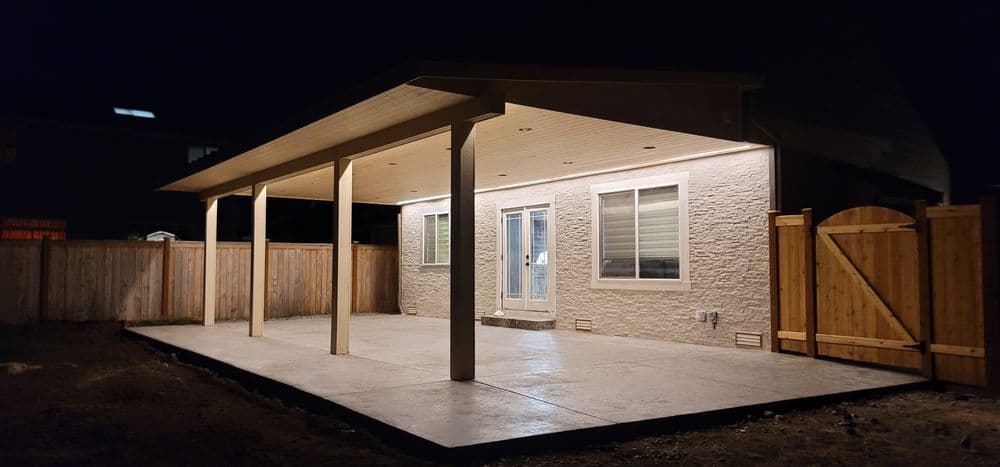 Modern backyard patio with pergola, ambient lighting, and fenced yard at night.