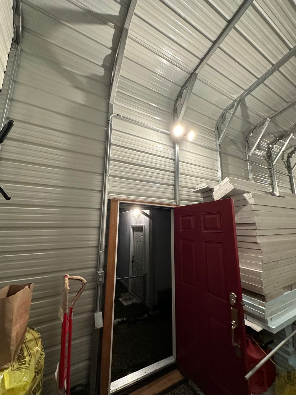 Interior view of a storage shed showing a red door and metal walls, with stacked panels inside.