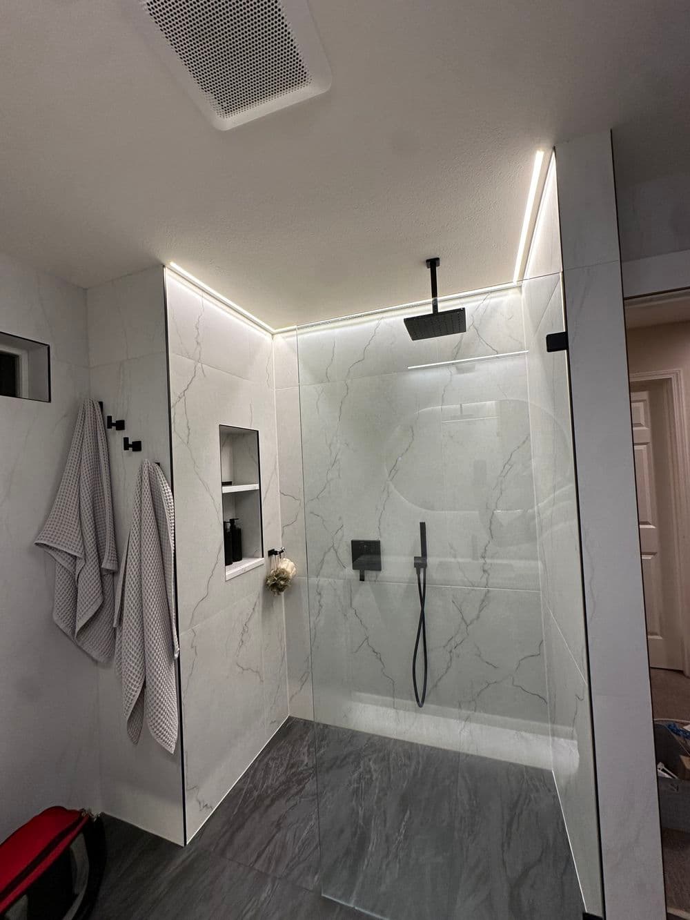 Modern bathroom shower with marble tiles, glass panel, and stylish black fixtures.