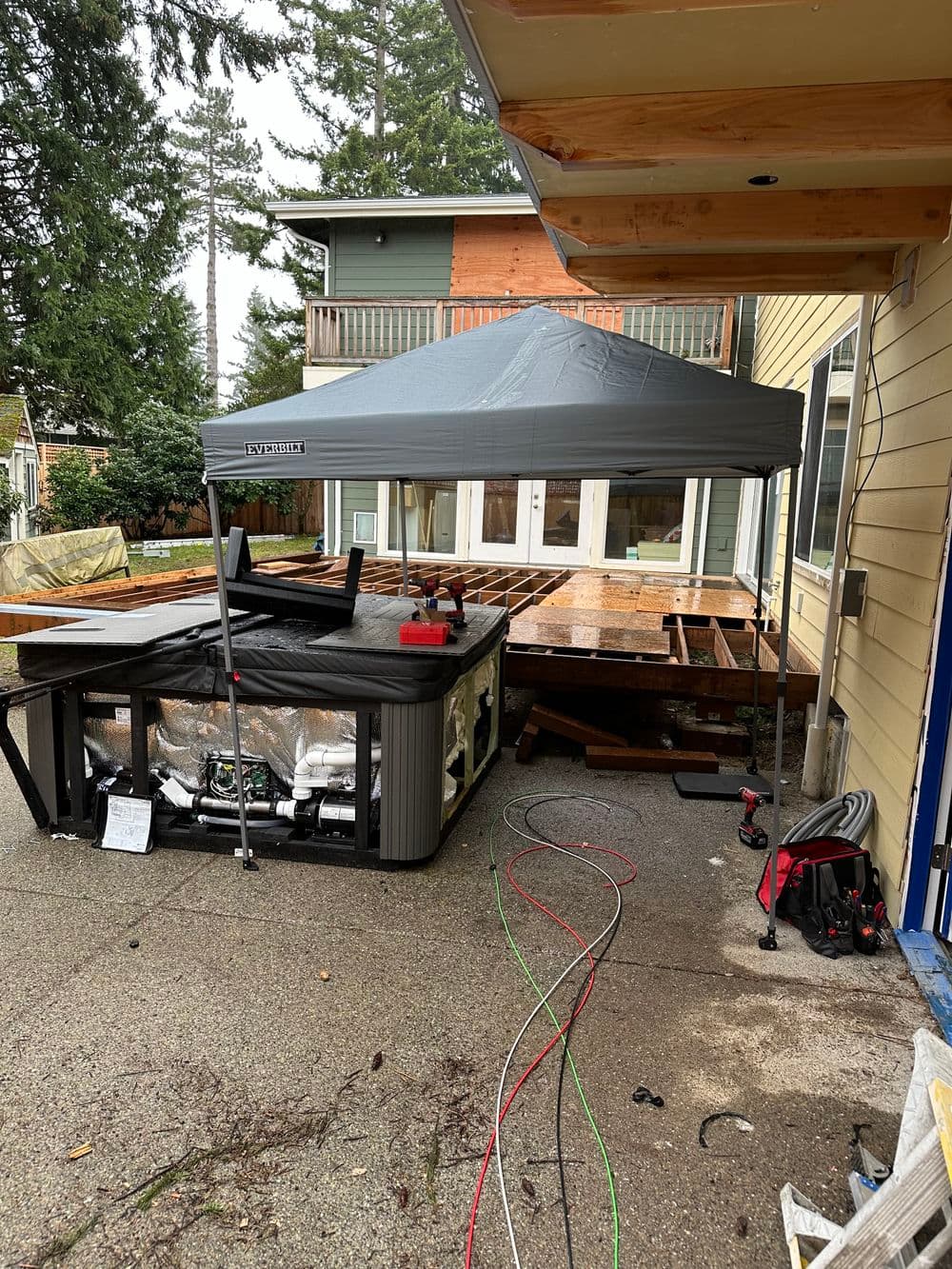 Construction site with a hot tub under a canopy, renovation of a home deck in progress.