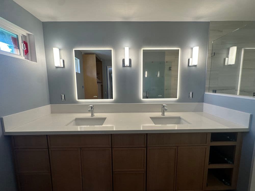 Modern bathroom with dual sinks, backlit mirrors, and contemporary lighting.