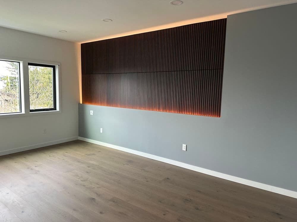 Modern living room with wooden accent wall and recessed lighting, featuring large windows.
