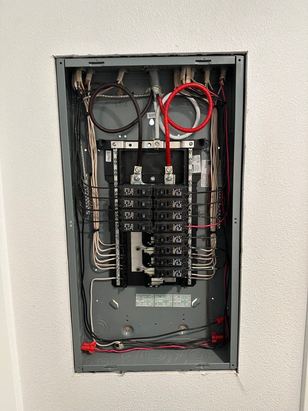 Electrical panel with multiple circuit breakers and wiring, installed in a wall.